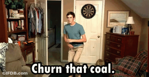A Man Standing In Front Of A Dart Board With The Words Churn That Coal Written Below Him GIF