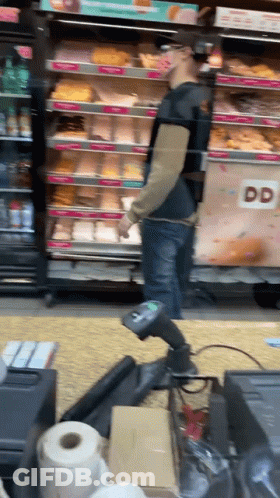 A Man Standing In Front Of A Dunkin Donuts Cooler GIF