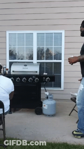 A Man Standing In Front Of A Grill With A Propane Tank In Front Of Him GIF