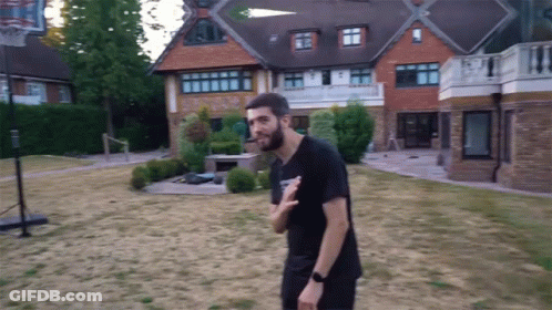 A Man Standing In Front Of A Large House With A Basketball Hoop In The Backyard GIF
