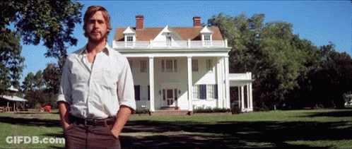 A Man Standing In Front Of A Large White House With His Hands In His Pockets GIF