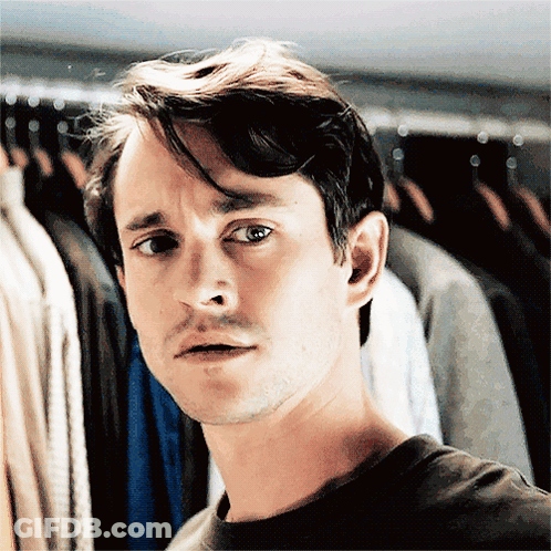 A Man Standing In Front Of A Rack Of Clothes Making A Face GIF