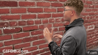 A Man Standing In Front Of A Red Brick Wall With A If.com Watermark GIF