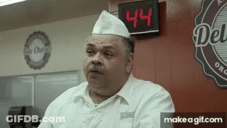 A Man Standing In Front Of A Sign That Says Deli GIF