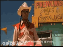A Man Standing In Front Of A Sign That Says Fireworks Snakes And Sparklers GIF