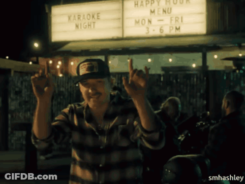 A Man Standing In Front Of A Sign That Says Happy Hour Menu GIF