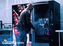 A Man Standing In Front Of A Vending Machine With A Coca Cola Advertisement On It GIF
