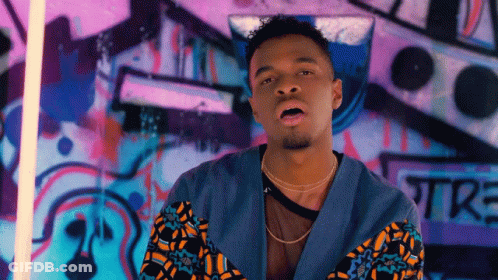 A Man Standing In Front Of A Wall With Graffiti On It That Says Tre GIF