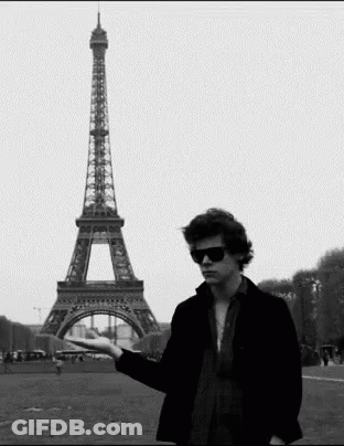 A Man Standing In Front Of The Eiffel Tower Holding Something In His Hand GIF