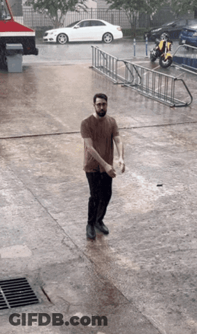 A Man Standing In The Rain With A Motorcycle Parked Behind Him GIF