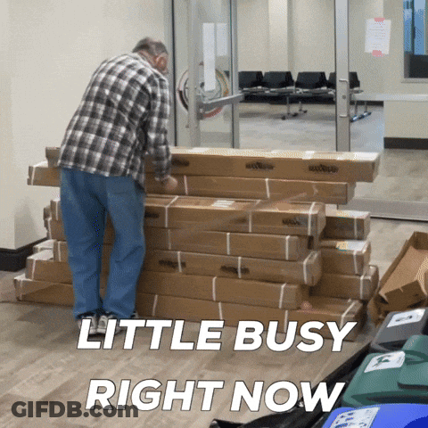 A Man Standing Next To A Pile Of Cardboard Boxes With The Words Little Busy Right Now Above Him GIF