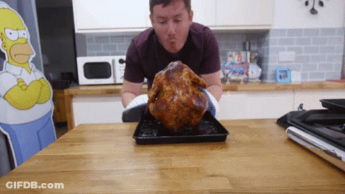A Man Standing Next To A Roasted Chicken On A Table GIF