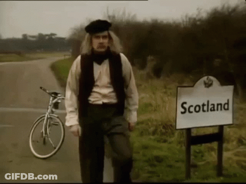 A Man Standing Next To A Sign That Says " Scotland " GIF