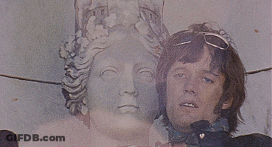 A Man Standing Next To A Statue With A Crown On His Head GIF