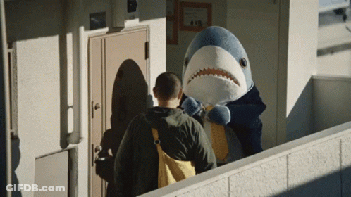 A Man Standing Next To A Stuffed Shark With A Backpack GIF
