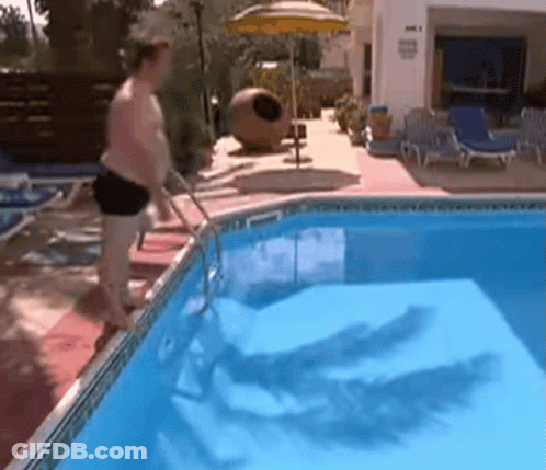 A Man Standing Next To A Swimming Pool With A Yellow Umbrella In The Background GIF