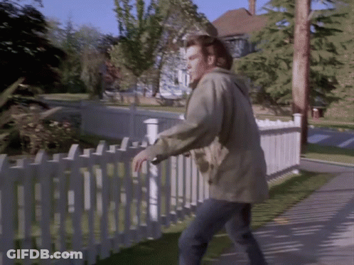A Man Standing Next To A White Picket Fence Looking Over It GIF