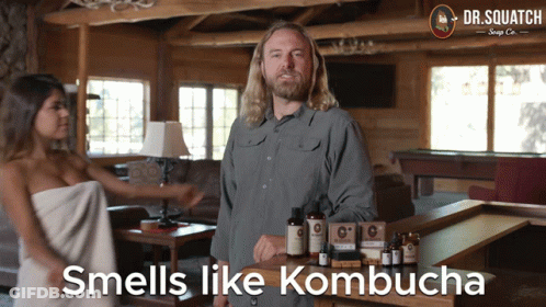 A Man Standing Next To A Woman Wrapped In A Towel With The Words " Smells Like Kombucha " Below Him GIF