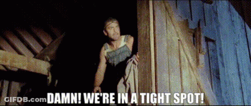 A Man Standing Next To A Wooden Wall With The Words Damn We 'Re In A Tight Spot . GIF