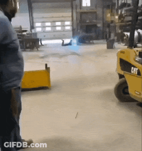 A Man Standing Next To A Yellow Cat Forklift In A Garage GIF