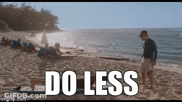 A Man Standing On A Beach Next To A Surfboard With The Words Do Less Written On It GIF