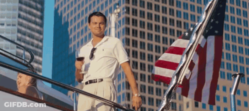 A Man Standing On A Boat Holding A Glass Of Wine In Front Of An American Flag GIF