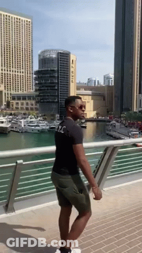 A Man Standing On A Bridge With A Building In The Background That Says Pier 7 On It GIF