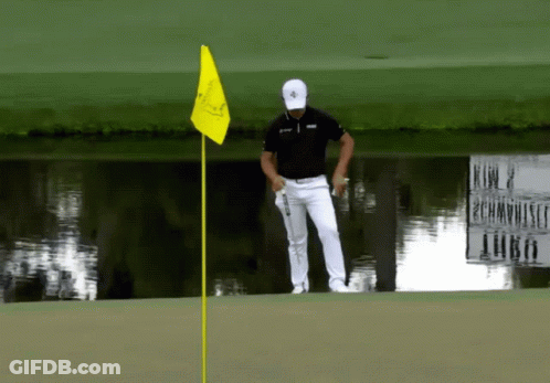 A Man Standing On A Golf Course With A Yellow Flag GIF