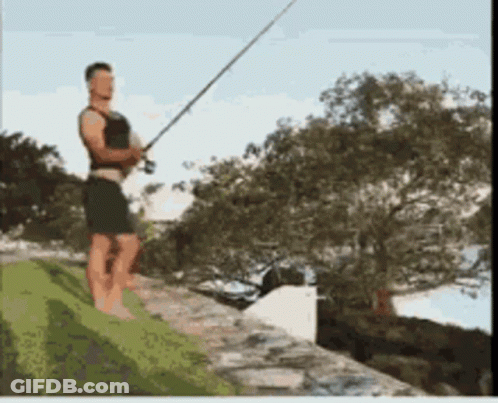 A Man Standing On A Ledge Holding A Fishing Pole GIF