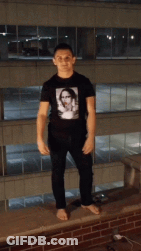 A Man Standing On A Ledge With His Arms Up GIF