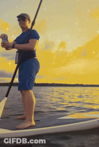 A Man Standing On A Paddle Board In The Water Holding A Can Of Bud Light GIF