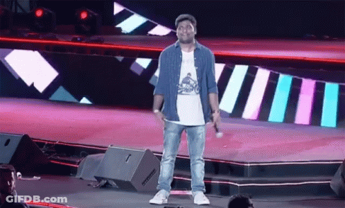 A Man Standing On A Stage With A Microphone In His Hand GIF
