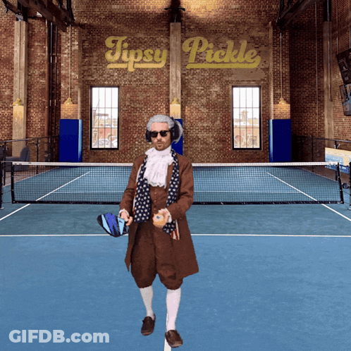 A Man Standing On A Tennis Court With A Sign That Says Tipsy Pickle Behind Him GIF