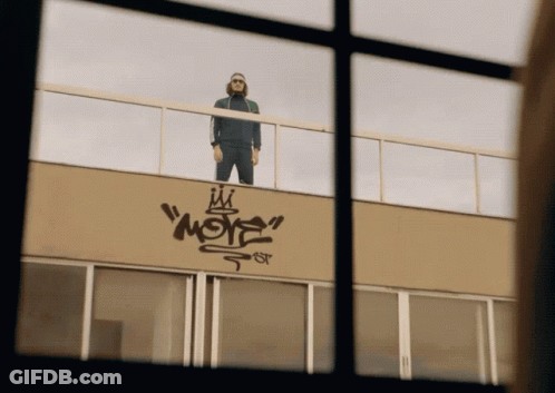A Man Standing On Top Of A Building With Graffiti On The Side That Says " More " GIF