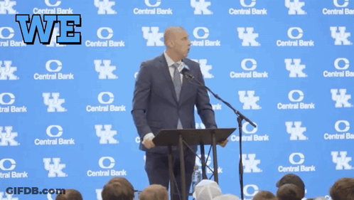 A Man Stands At A Podium In Front Of A Wall With Central Bank Logos On It GIF