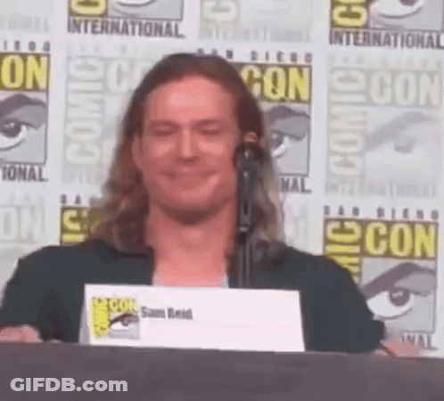 A Man Stands At A Podium With A Comic Con Sign In The Background GIF