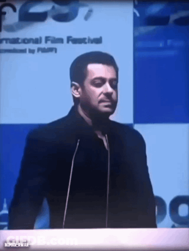 A Man Stands At A Podium With A Sign That Says International Film Festival GIF