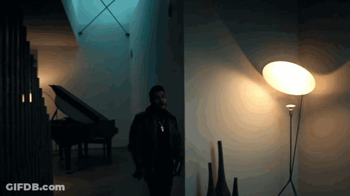 A Man Stands In A Dark Room With A Lamp And A Piano GIF