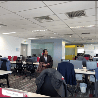 A Man Stands In An Office With A Sign That Says Osama Tahir On It GIF
