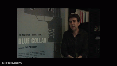 A Man Stands In Front Of A Blue Collar Poster GIF