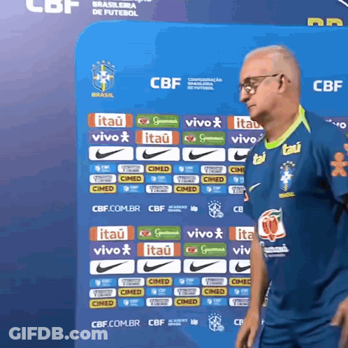 A Man Stands In Front Of A Blue Wall With Logos For Itau And Vivo GIF