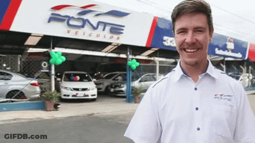 A Man Stands In Front Of A Car Dealership Called Fonte GIF