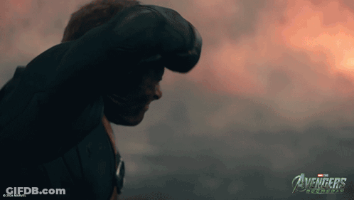 A Man Stands In Front Of A Cloudy Sky With The Avengers Logo On The Bottom GIF