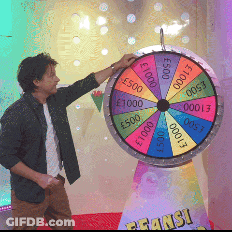 A Man Stands In Front Of A Colorful Spinning Wheel That Says ' Fransi ' On It GIF