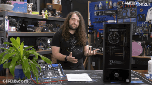A Man Stands In Front Of A Computer With The Words Gamers Nexus Written On The Wall Behind Him GIF