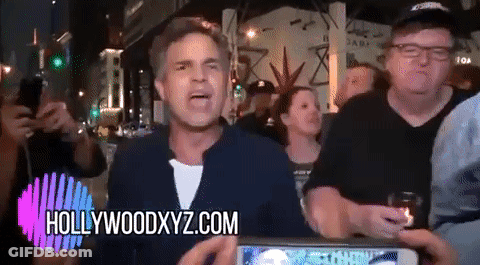 A Man Stands In Front Of A Crowd With Hollywoodxyz.com On The Bottom Right GIF