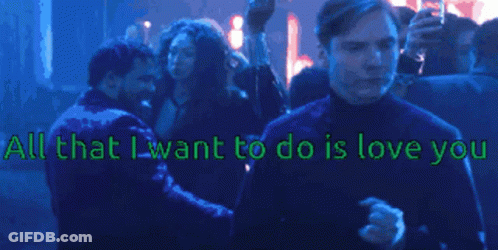 A Man Stands In Front Of A Crowd With The Words " All That I Want To Do Is Love You " Above Him GIF