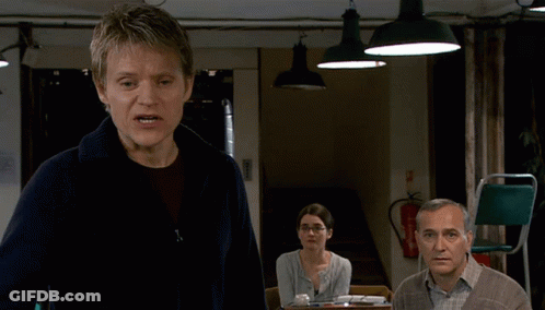 A Man Stands In Front Of A Fire Extinguisher And A Woman Sitting At A Table GIF