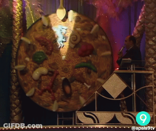 A Man Stands In Front Of A Giant Pizza With The Number 9 On The Bottom GIF