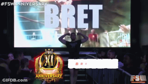 A Man Stands In Front Of A Large Screen That Says Bret On It GIF